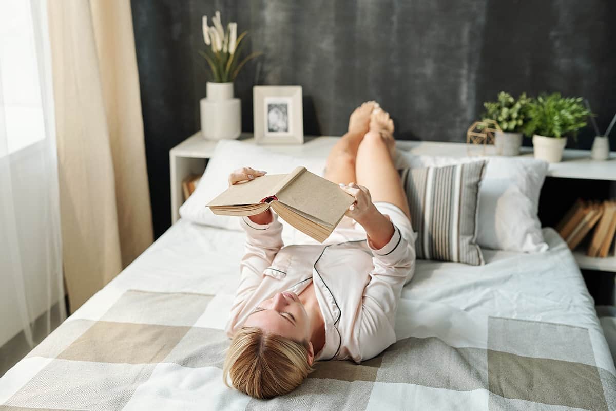 girl reading book in bed lying on back